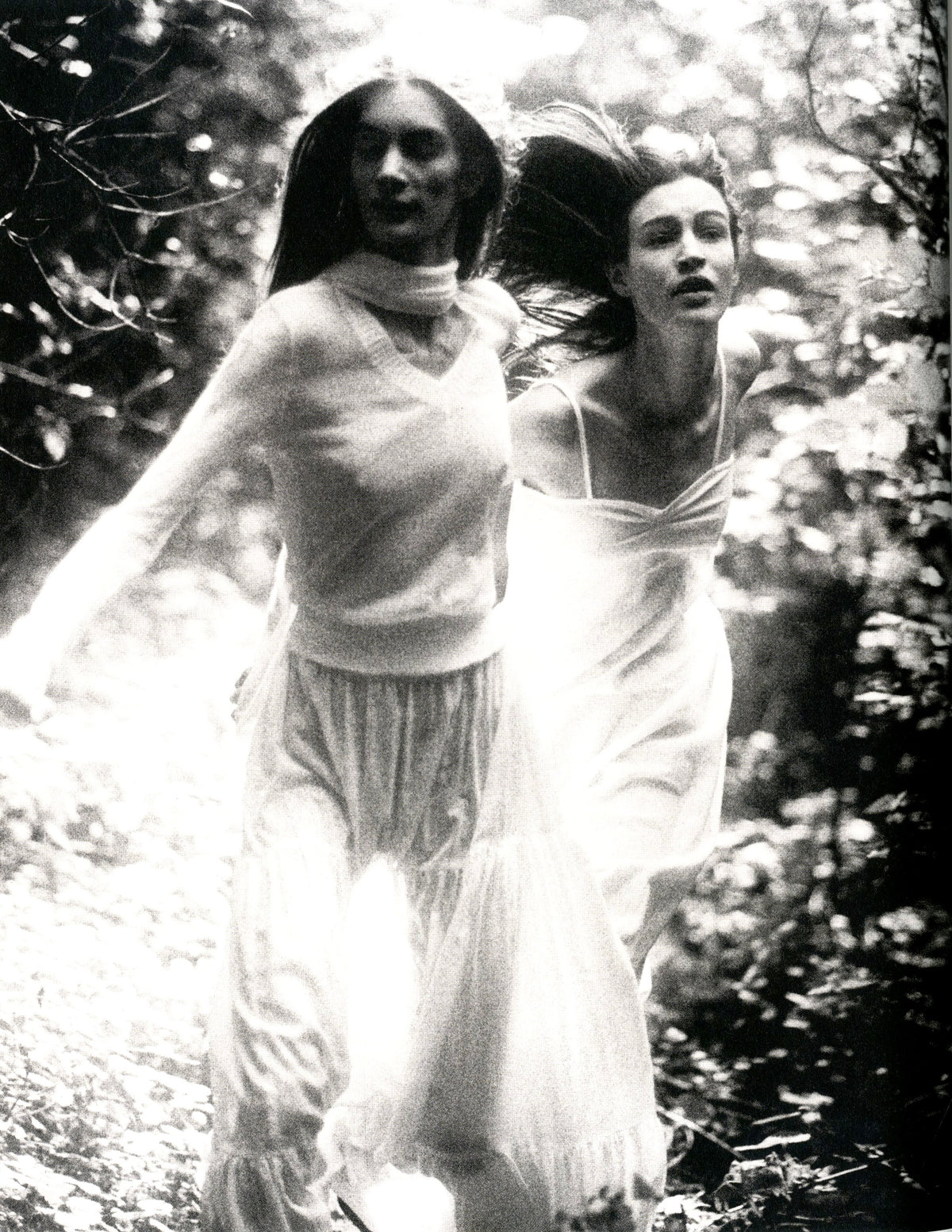 Black-and-white photograph from 6+ Antwerp Fashion: two women in long white dresses running through woods.
