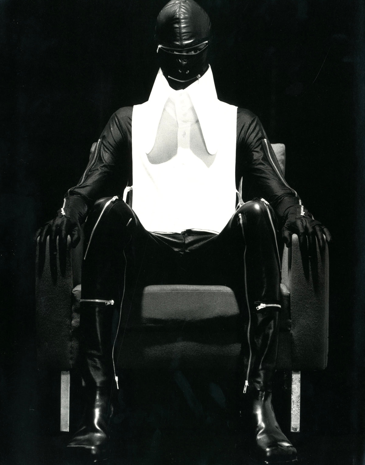 Image from A Magazine N°A: seated figure in black with covered head and a white bib collar against a dark ground.