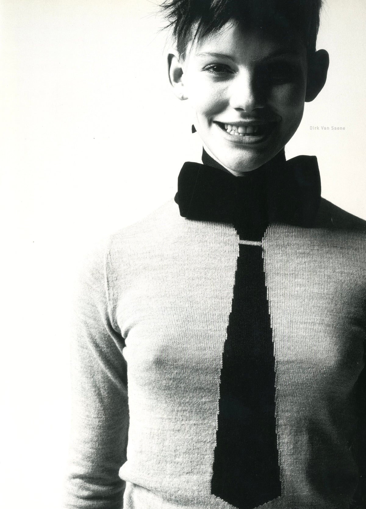 Photograph from A Magazine N°A: smiling young model in a knit sweater with an oversized black bow and tie.