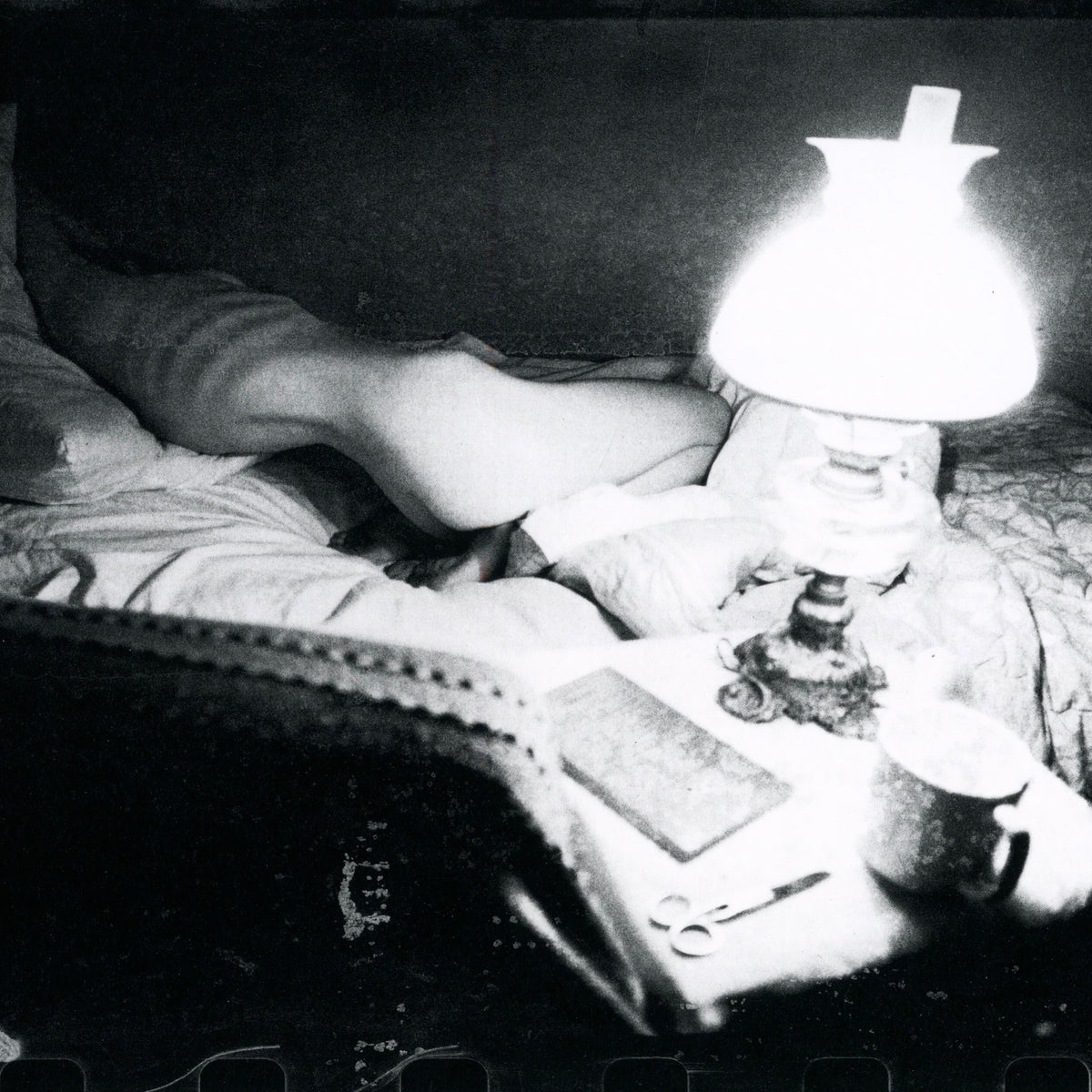 Black and white photograph of a bedroom illuminated by a bedside lamp. intermission books.
