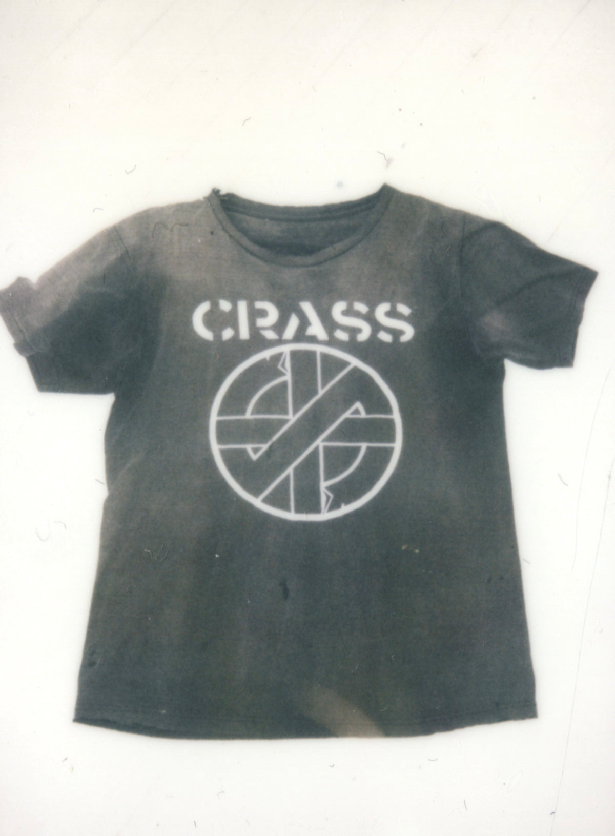 Faded black vintage Crass T-shirt with stencil logo and circular symbol, laid flat.