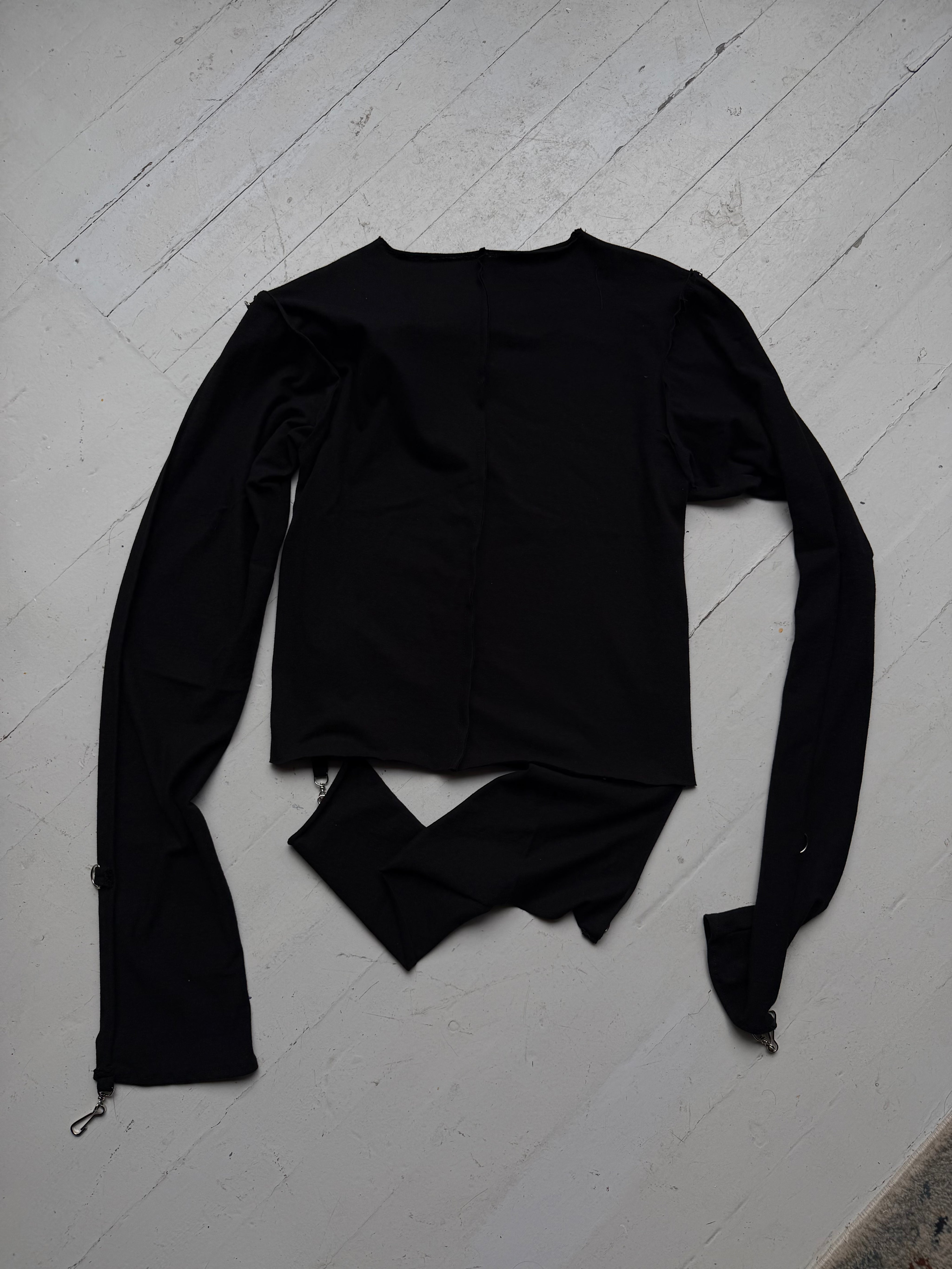 Back of the intermission black long-sleeve top showing the cut, separated hem.