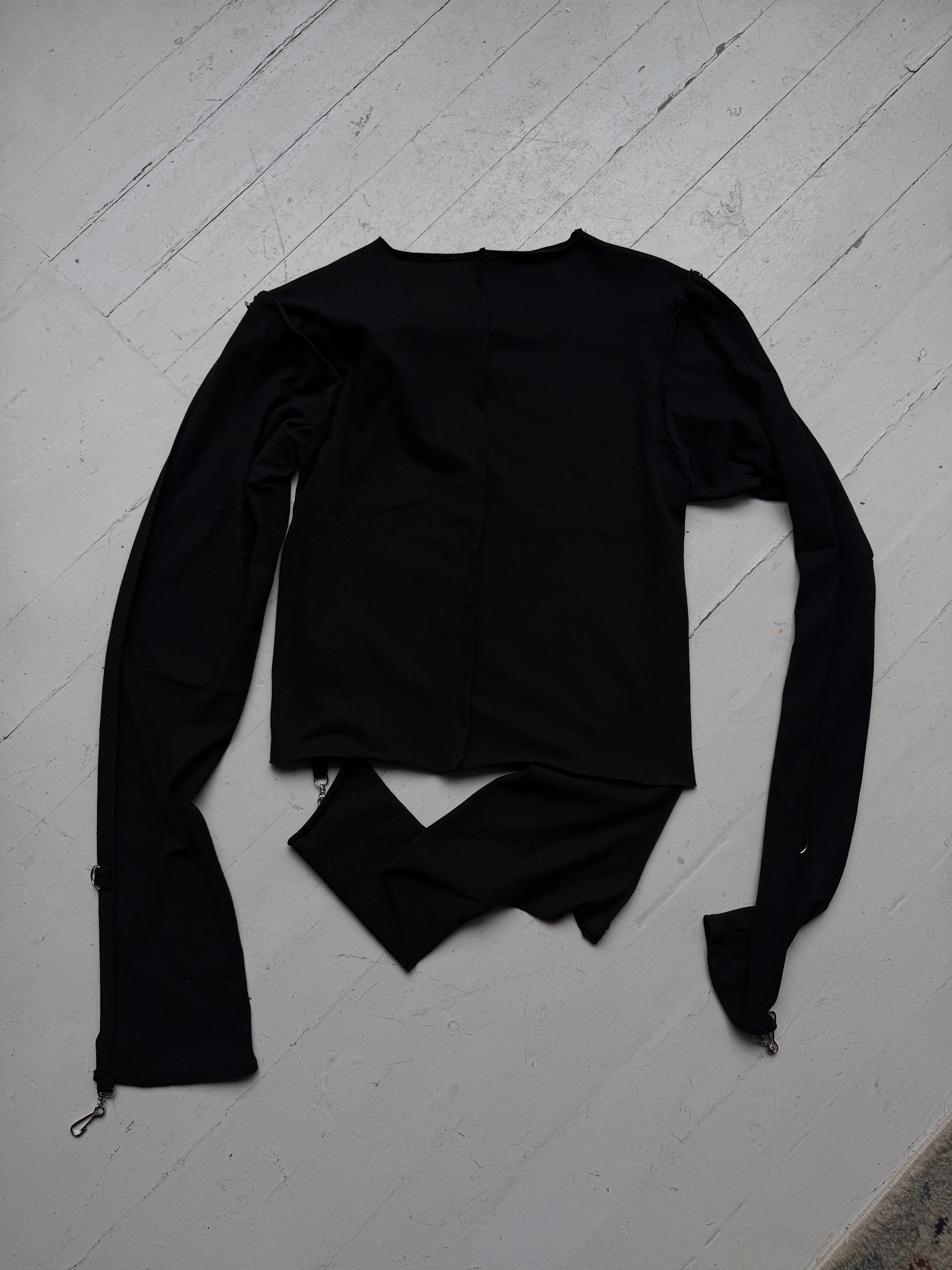 Back of the intermission black long-sleeve top showing the cut, separated hem.