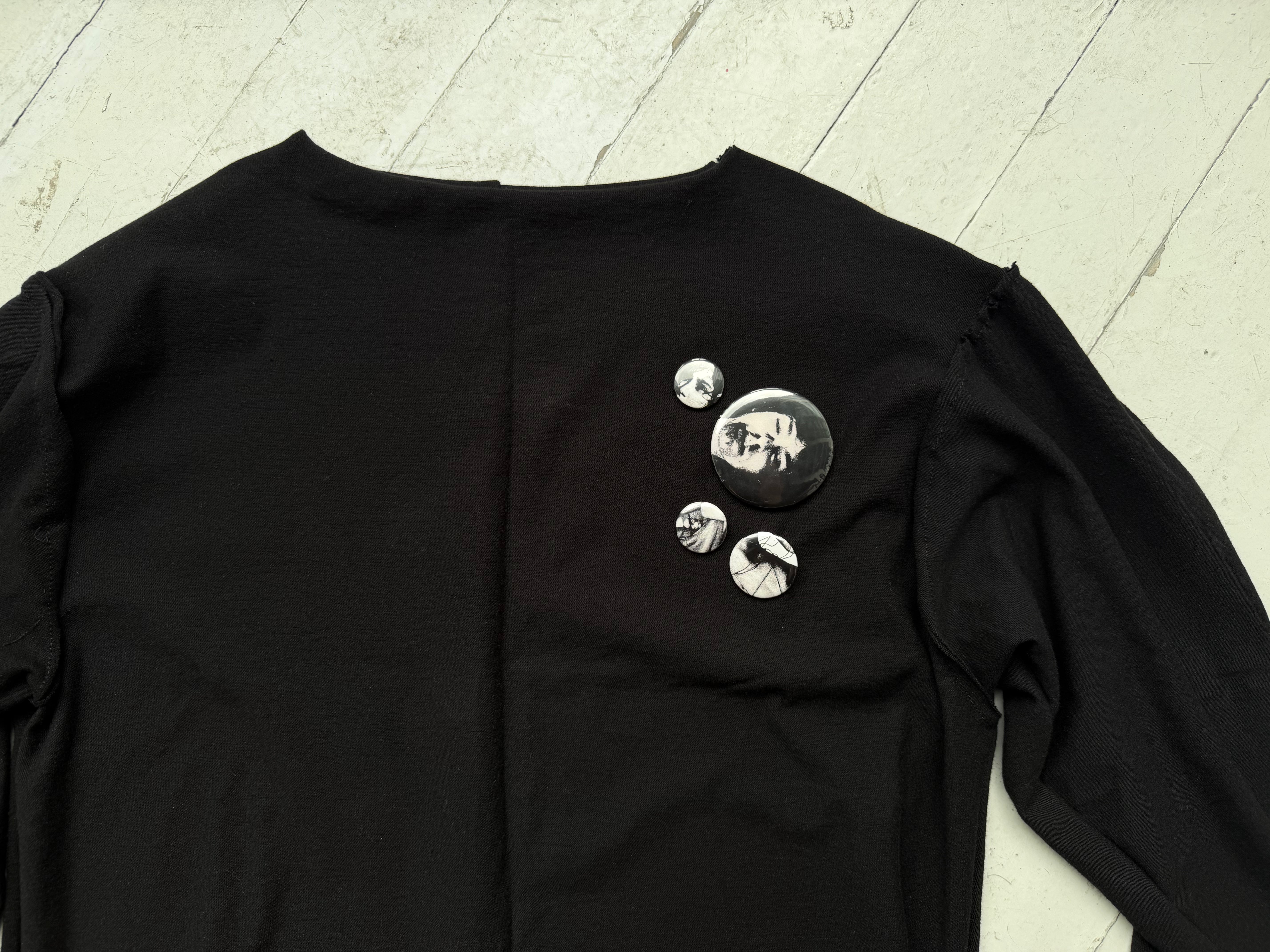 Close-up of three hand-sewn pin-back buttons on the chest of the intermission black top.