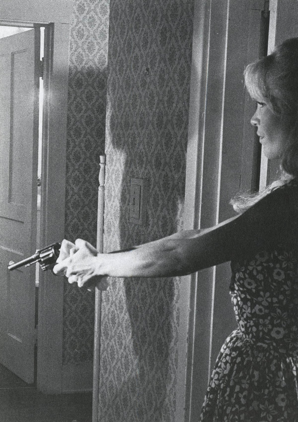 Woman in a patterned dress at a doorway with her arm extended, film-still style image from Fama & Fortune Heft 8.