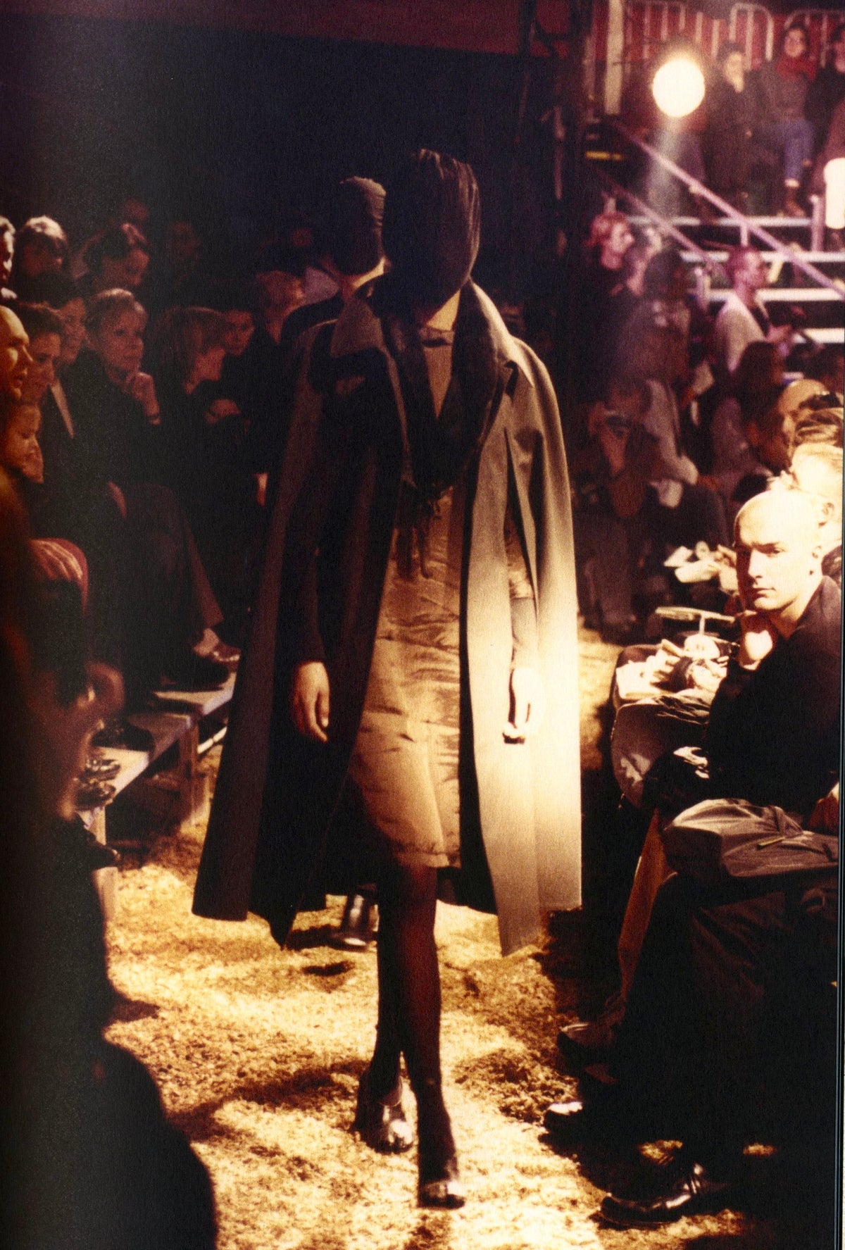 Model in a long coat walking through a crowd at night under show lights, Maison Martin Margiela ‘20’ catalogue.
