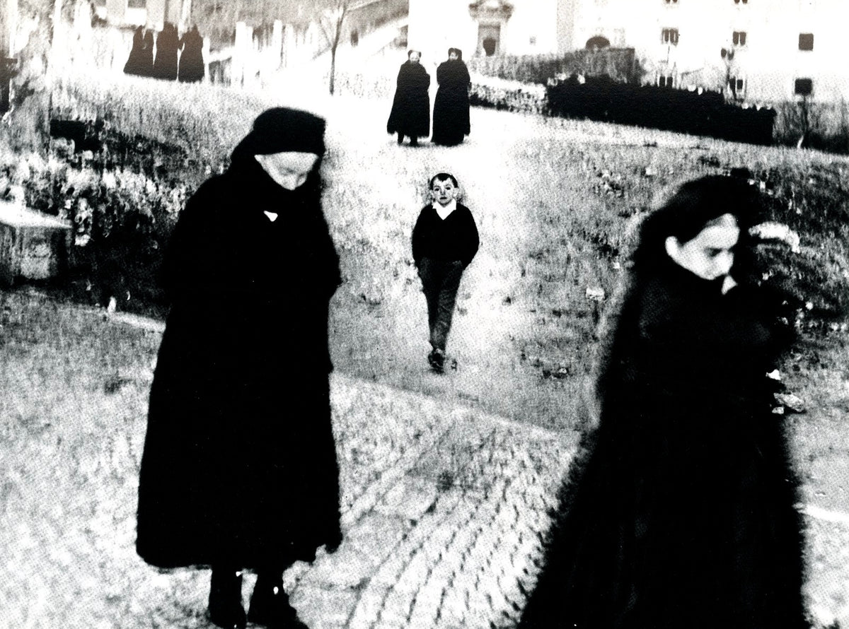 Mario Giacomelli photograph: women in black shawls and a small boy on a village street, high-contrast black and white.