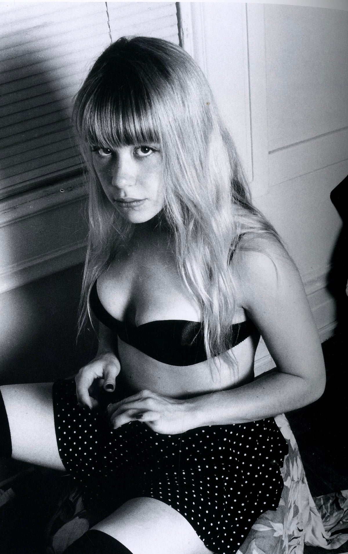 Blonde young woman with bangs seated in a black bra and polka-dot skirt, from XX Girls by Richard Kern.