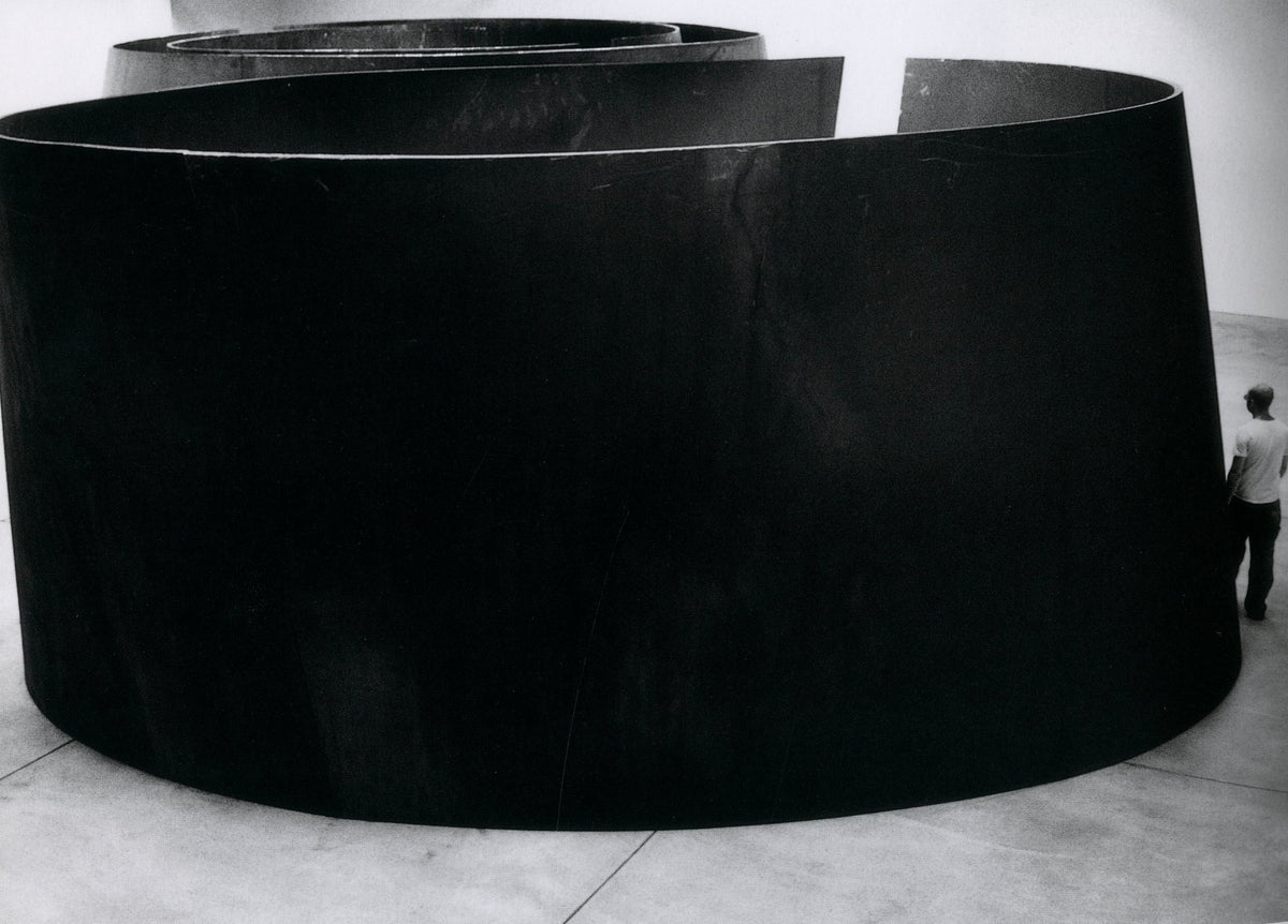 A curved steel plate being moved by heavy machinery inside an industrial hall, Richard Serra: Torqued Ellipses.