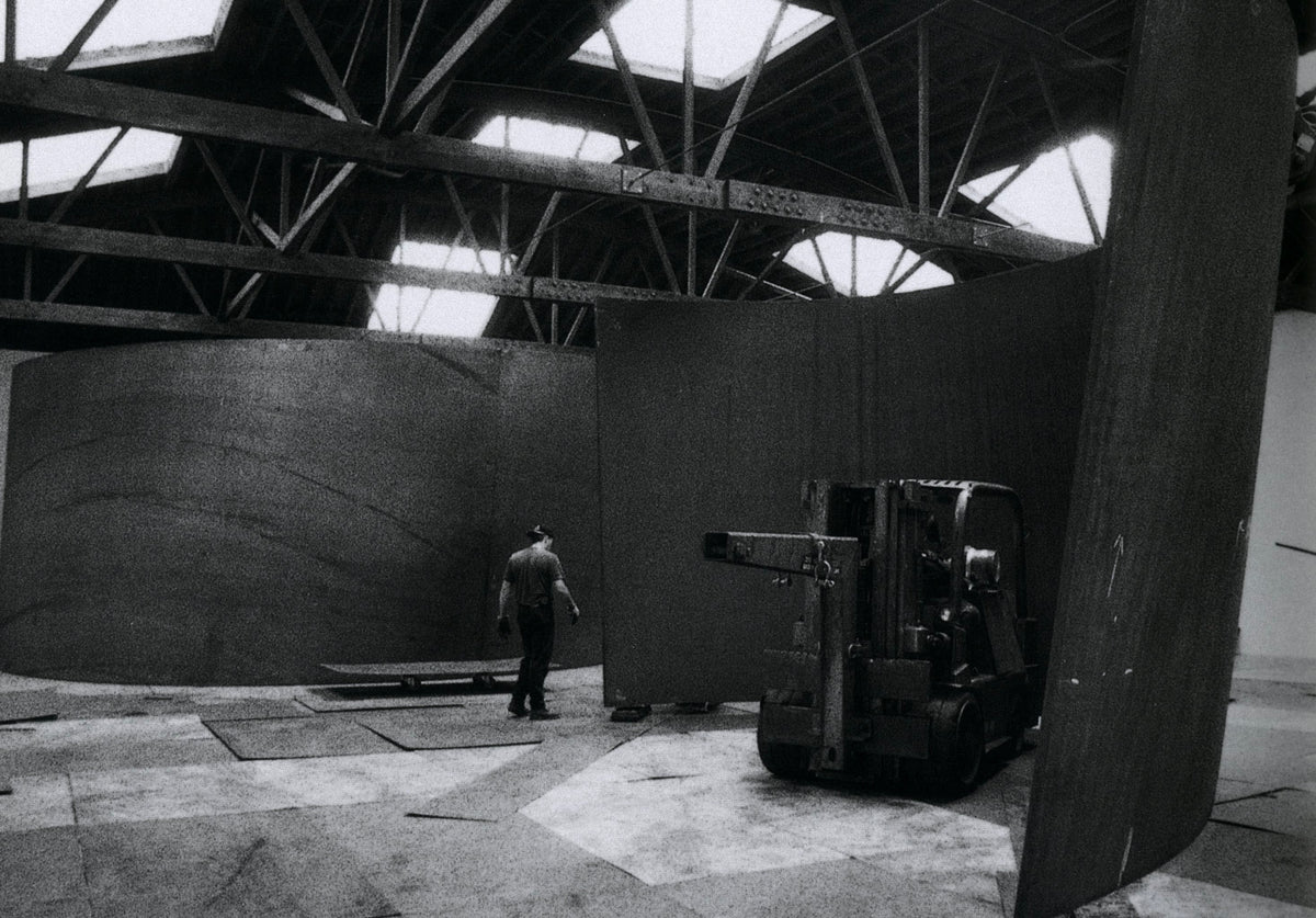 Dark steel torqued ellipse in a white gallery with a visitor for scale, Richard Serra: Torqued Ellipses.