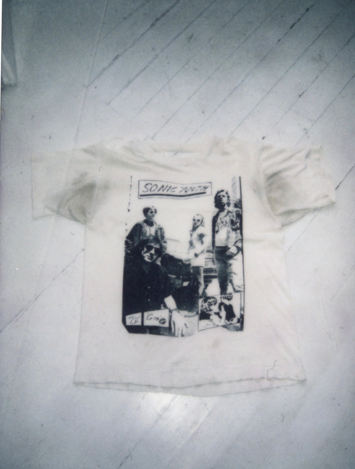 Front of a vintage white Sonic Youth T-shirt with a black-and-white band photo print, laid flat on a wooden floor.